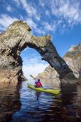 Sea kayaking beneath a natural arch near Sturrall, Glencolmcille, County Donegal, Ireland.