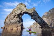 Sea kayaking beneath a natural arch near Sturrall, Glencolmcille, County Donegal, Ireland.