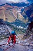 Walker climbing ladders above Argentiere, Tour of Mt Blanc, French Alps, France.