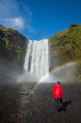 Rainbow and person beneath 60m-high Skogafoss waterfall. Skogar, Sudhurland, south Iceland.