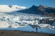 Person beside Fjallsarlon iceberg lagoon, beneath Fjallsjokull glacier, Sudhurland, Iceland.