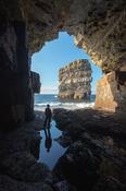 Person viewing Dun Briste sea stack from a cave beneath Downpatrick Head. County Mayo, Ireland.