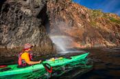 Sea kayaker beside a blow-hole rainbow, Arranmore Island, County Donegal, Ireland.
